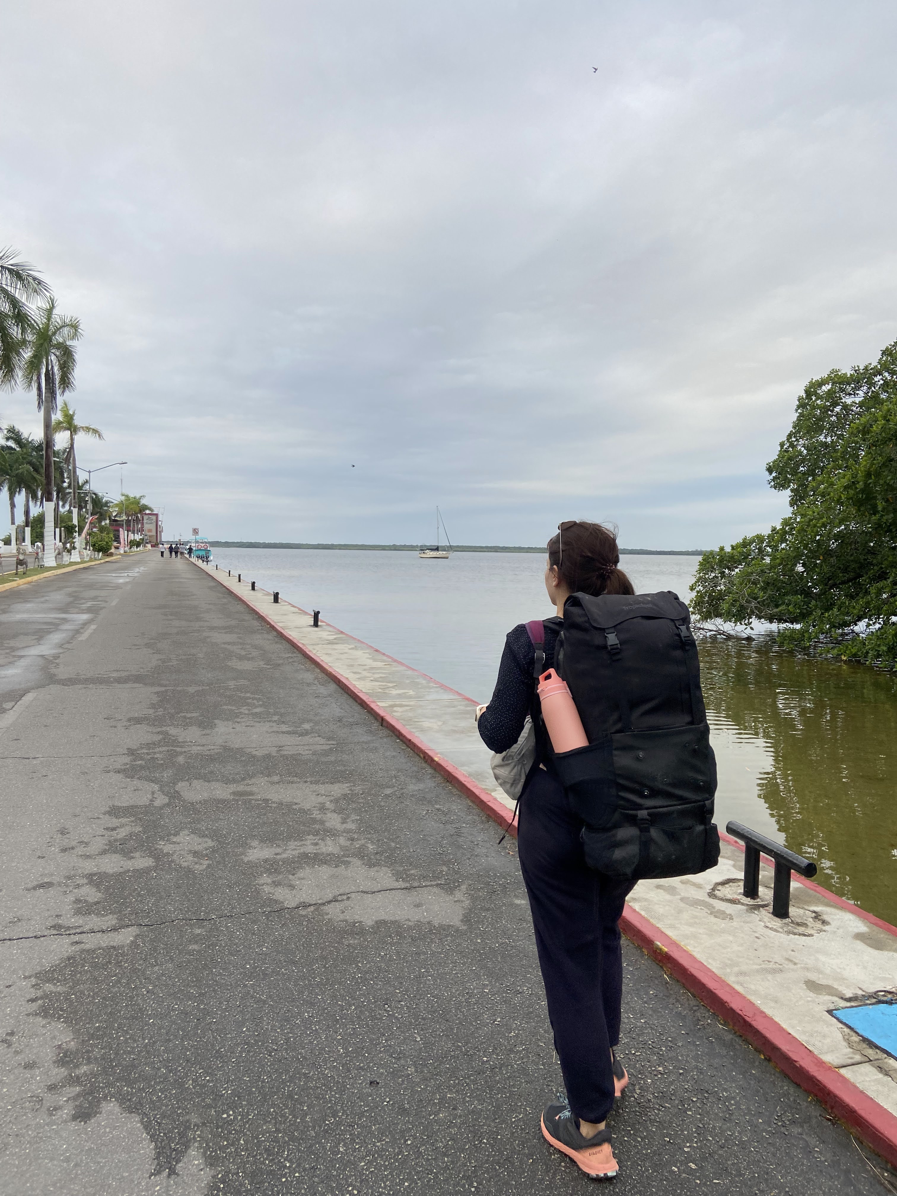 Digital Nomad woman with a backpack walking along a peaceful pier overlooking a calm bay, embodying the freedom of remote work
