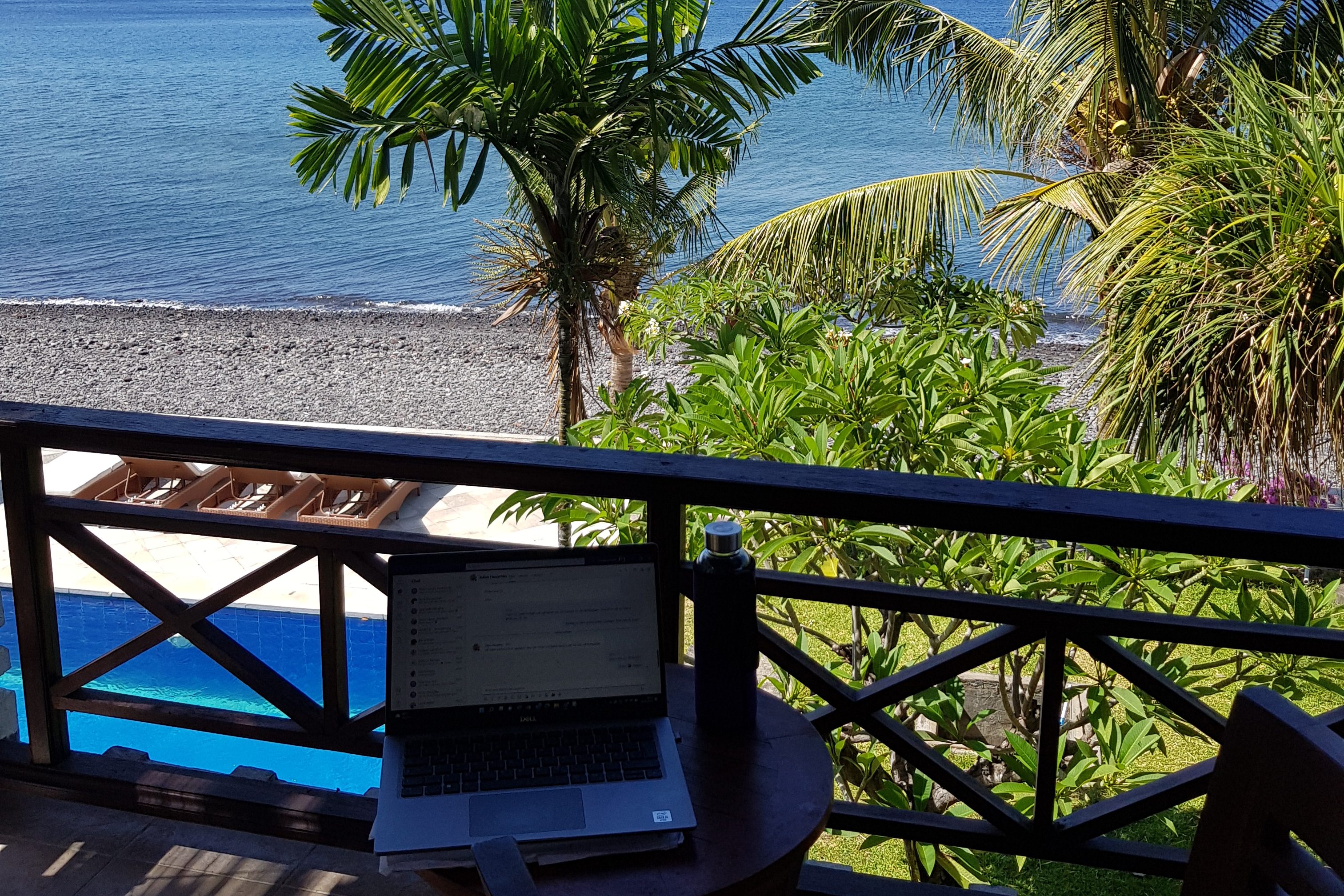  A laptop on a balcony with a view of palm trees and a beach in Bali, showing "what is a digital nomad" work setup