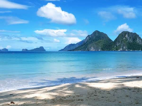 Pristine beach with turquoise waters and mountain backdrop in El Nido, Philippines, under a bright blue sky
