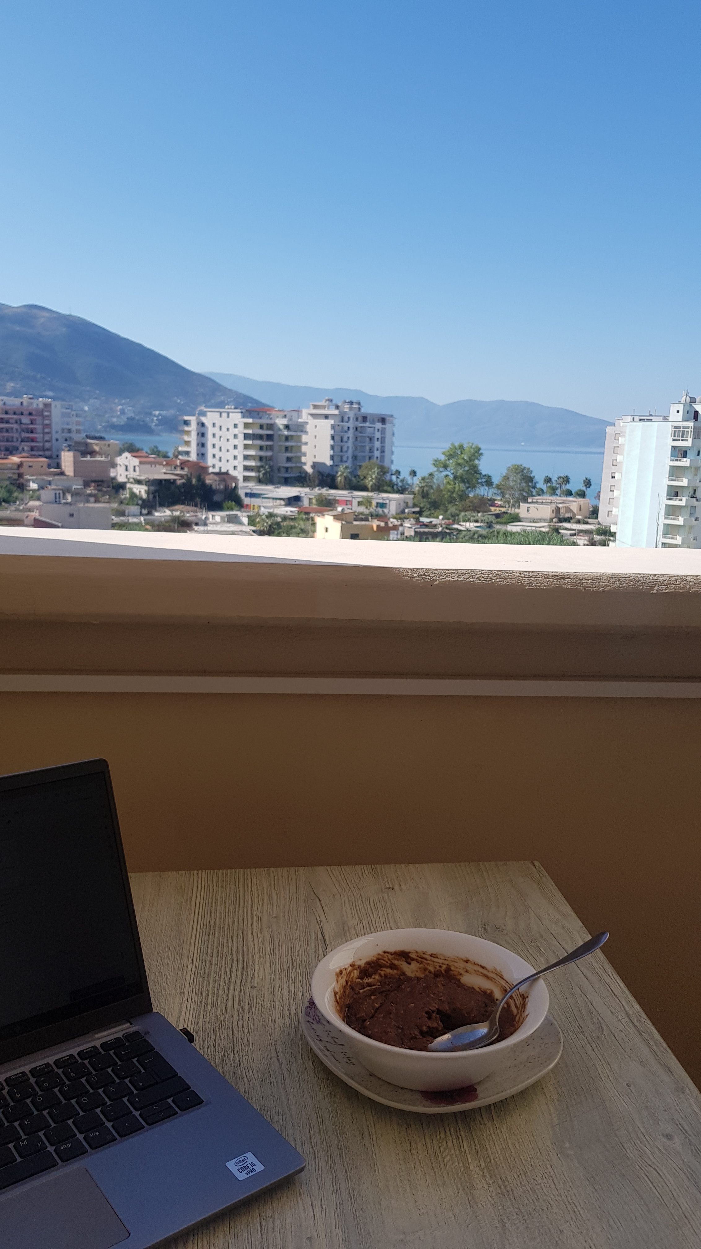 Laptop and breakfast on a balcony overlooking the city, mountains ans sea in Vlora, Albania, a typical digital nomad setup.