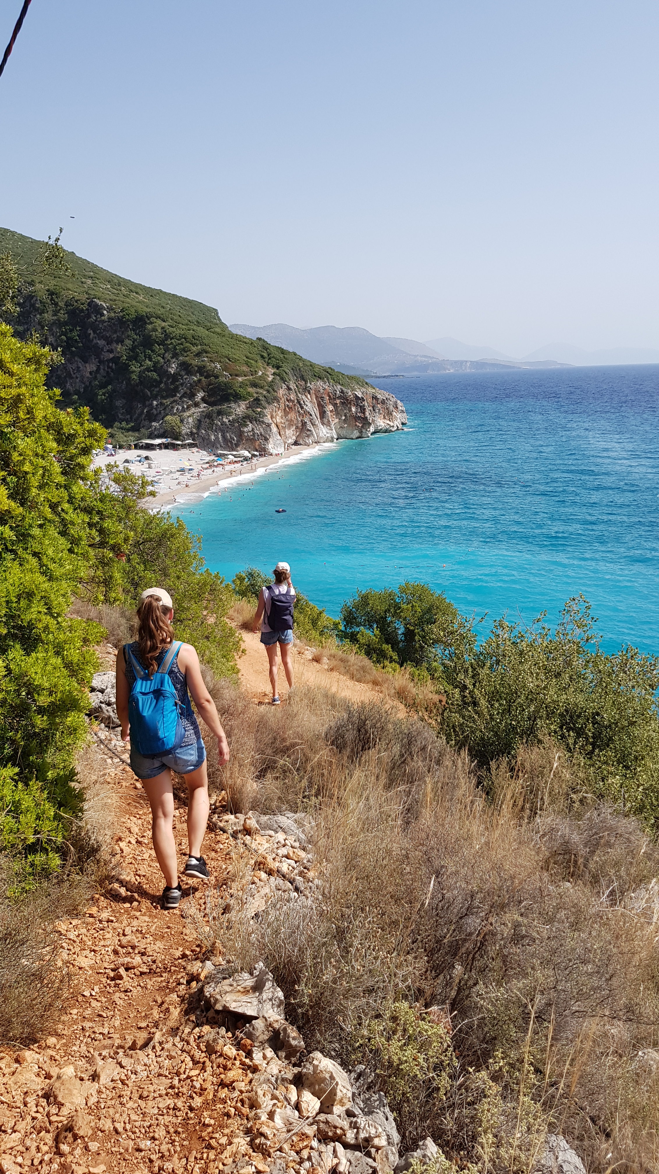 Two women hiking on a coastal trail near Gjipe Canyon in Albania, with a view of a beautiful beach, popular among digital nomads