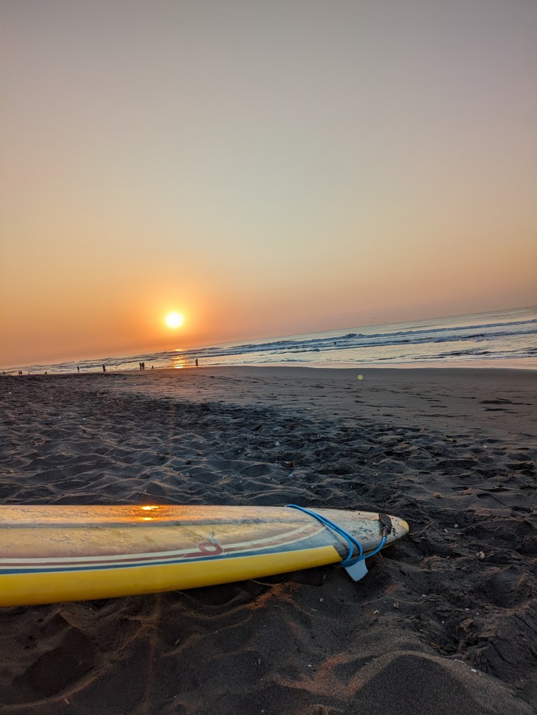 Sunset over the beach with a surfboard, a tranquil evening for digital nomads in El Paredon, Guatemala.
