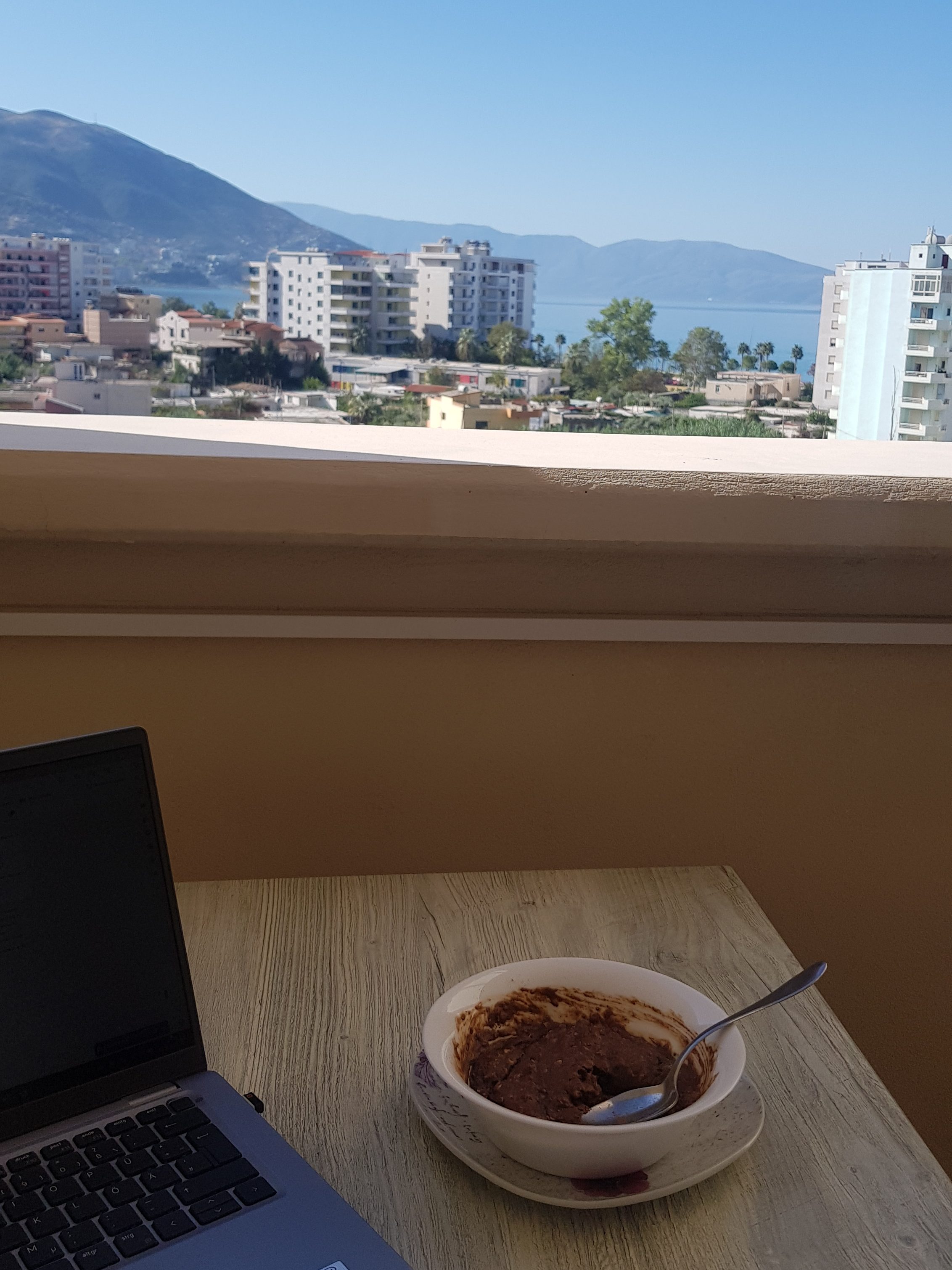 A laptop and coffee on a balcony overlooking the Albanian coastline, illustrating remote work in "what is a digital nomad" life.