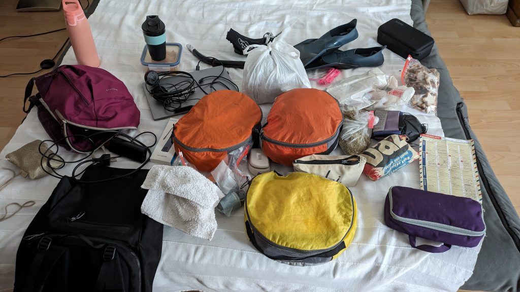 best backpacking essentials - bags, snorkel gear, laptop, brush, laid out on a white sofa