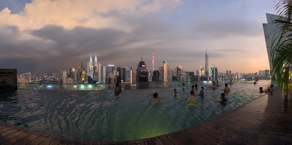 A rooftop infinity pool with a view of Kuala Lumpur's skyline at sunset, showcasing urban luxury in "how to become a digital nomad.