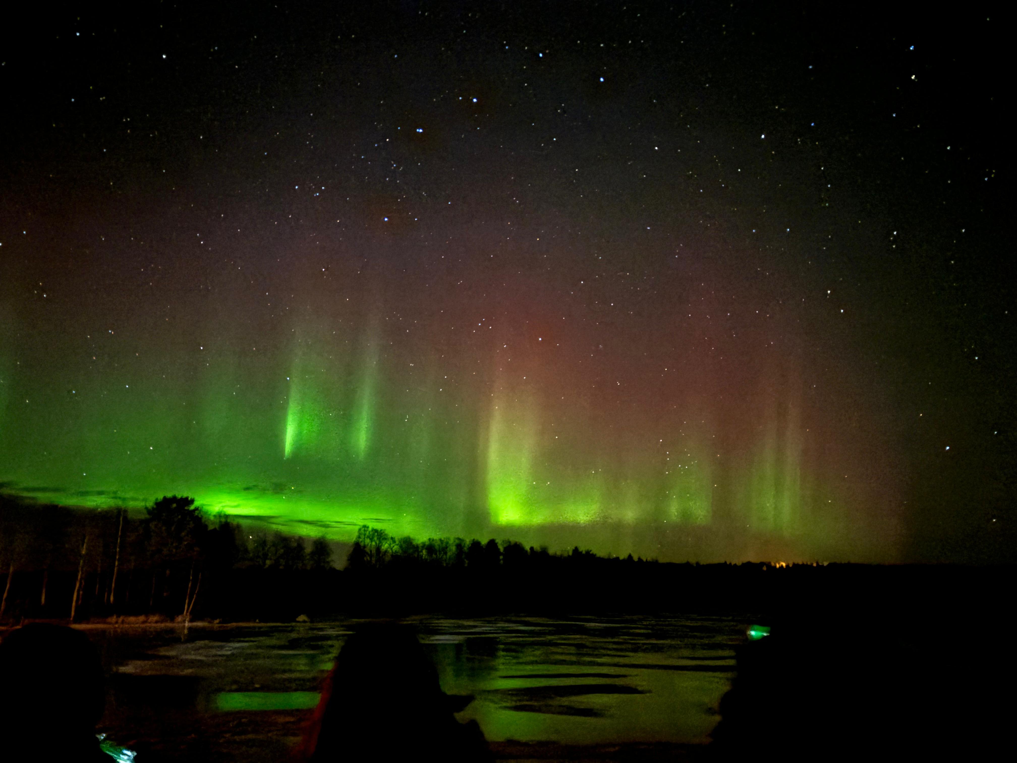 Vivid Northern Lights reflecting over a frozen lake near Rovaniemi, Lapland, Finland.