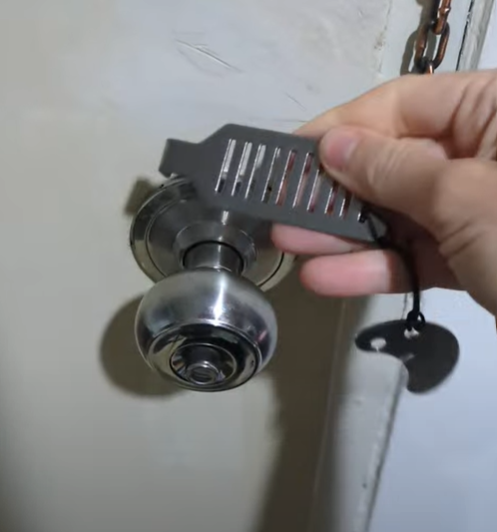A person demonstrating how to use a travel door lock by inserting it into the door frame near a doorknob.