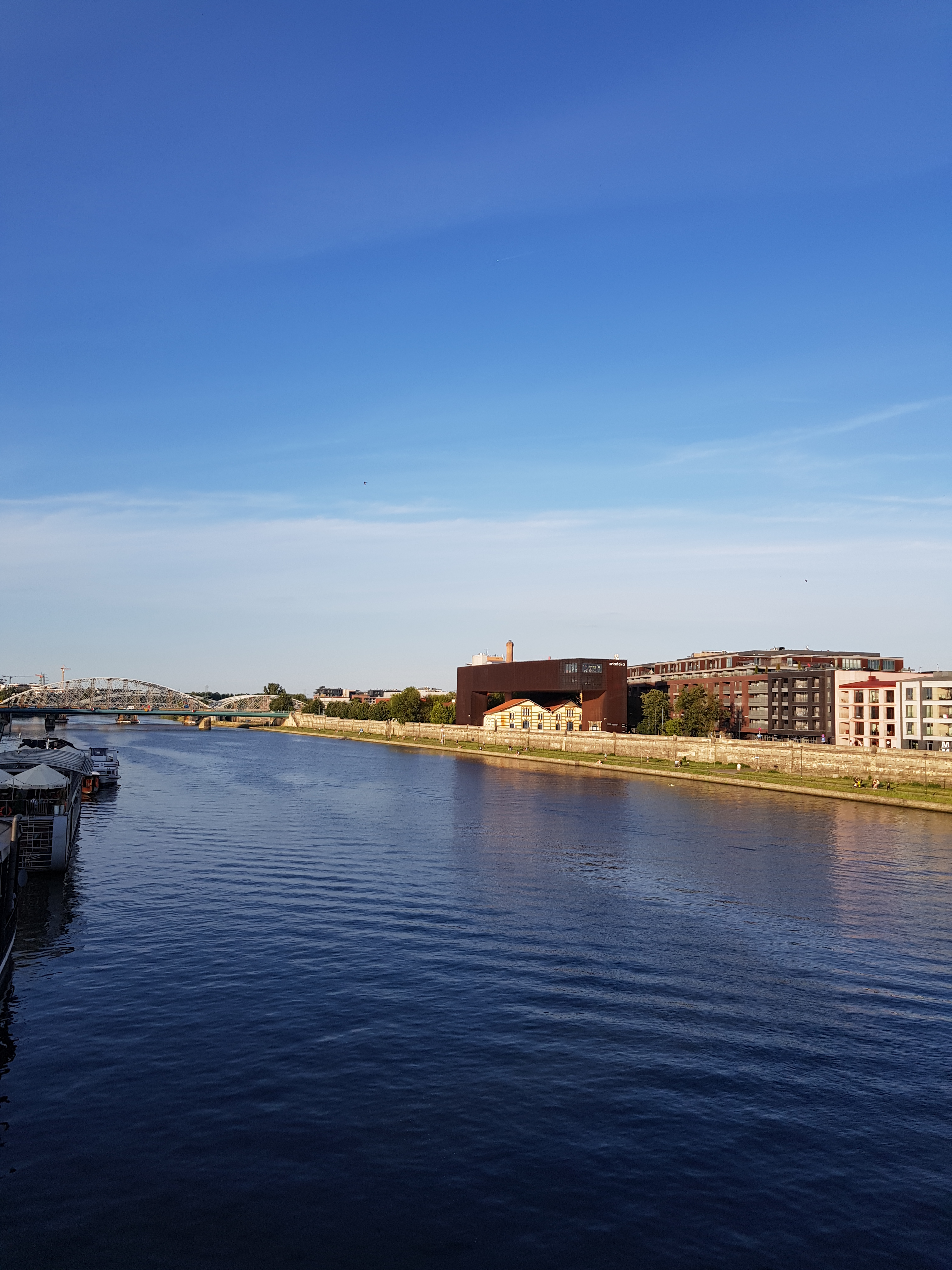 Sunlit Vistula River embankment in Kraków with riverside path for digital nomads